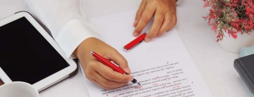 person proofreading a paper with a red pen