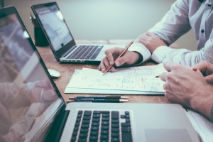 two people writing in between two laptop computers
